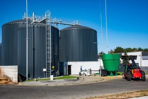 Widok na biogazownię z większej odległości. Widać zbiorniki fermentacyjne, zielony podajnik i fragmenty infrastruktury technicznej.